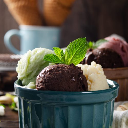 Three scoops of Vanilla pistachio and chocolate icecream balls in clay bowls on wooden kitchen table